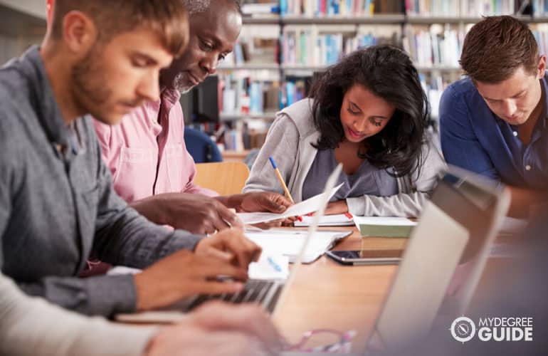 a group of adult students gathered around a table working on a project in a university library