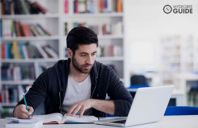 male student studying on his laptop in the library