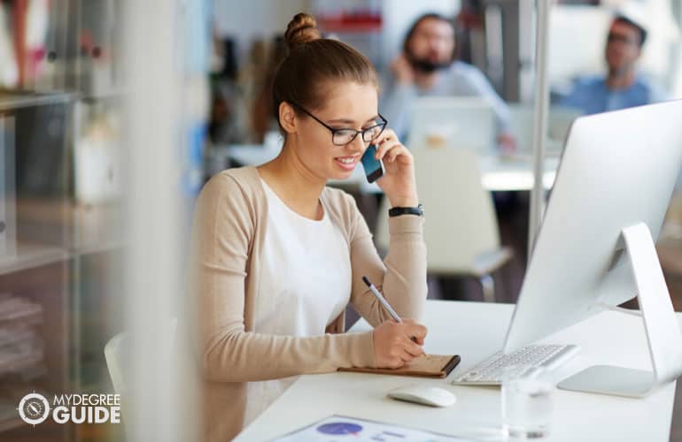 female professional talking on phone making notes on small notebook