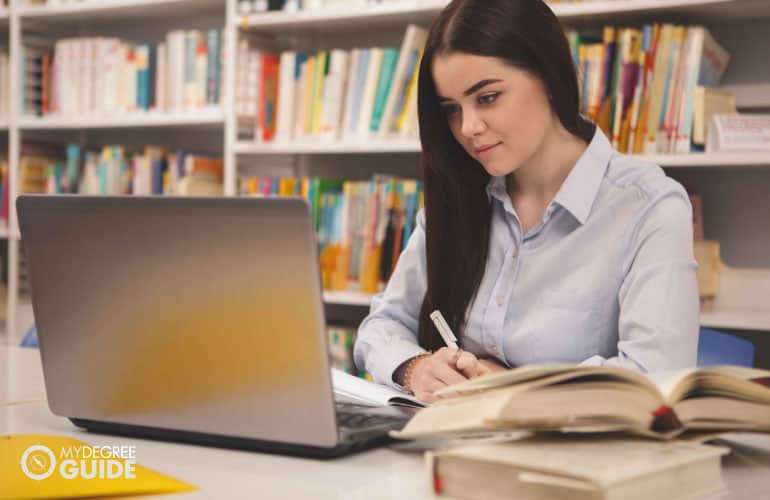 student studying in the library with a laptop and books