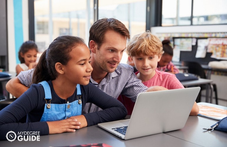 elementary education teacher helping his students during computer class