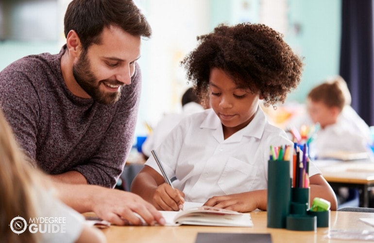 Elementary Education Teacher helping his student in writing