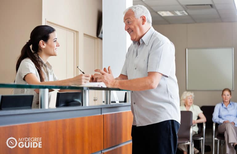 front desk personnel of a nursing home talking to an elderly man