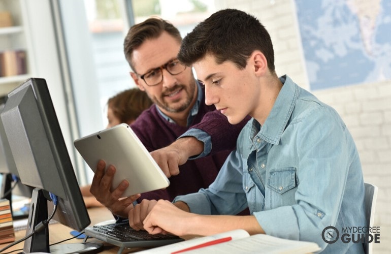 High school teacher assisting his student during computer class