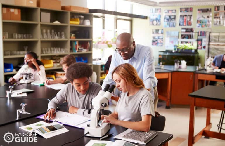 science teacher checking his student's work during Biology class